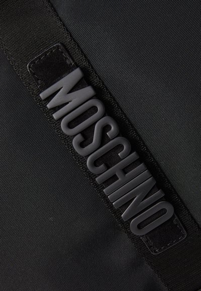 Czarna torba z tkaniny z teksturowanym, wypukłym logo "Moschino" z czarnej gumy na czarnym pasku. Gładka powierzchnia z delikatnym połyskiem.