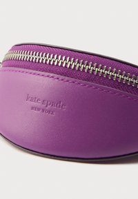 Fialové kožené puzdro so strieborným zipsom, na ktorom je vyrazené logo značky. Hladká textúra s zaobleným tvarom a kontrastným šitím.