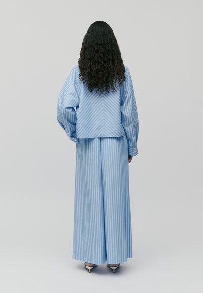 Blusa oversize a righe blu chiaro con maniche lunghe, abbinata a una gonna lunga coordinata. Entrambi i capi presentano righe verticali.