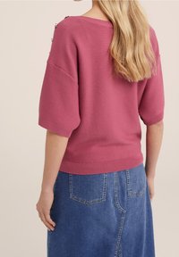 Kortärmad rosa tröja med texturerad stickning, som har metalliska detaljer och en avslappnad passform, matchad med en denimkjol.