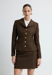 Hnědý tweedový blejzr s peplum střihem a zlatými knoflíky, v kombinaci s odpovídající sukní. Má klopový límec a jemnou texturu.