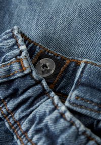 Denim tkanina u svijetloplavoj boji s narančastim šavovima. Ima nabran pojas i prozirni gumb s cvjetnim uzorkom na vrhu.