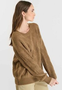 Brun stickad tröja med en lös passform, som har ett texturerat mönster och vida ärmar. Rundad halsringning och en mjuk, bekväm look.