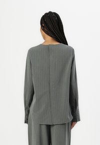 Grå langermet bluse med vertikale striper, rund halslinje, detalj på bakseam og mansjetter med knapper. Glatt stoff og avslappet passform.