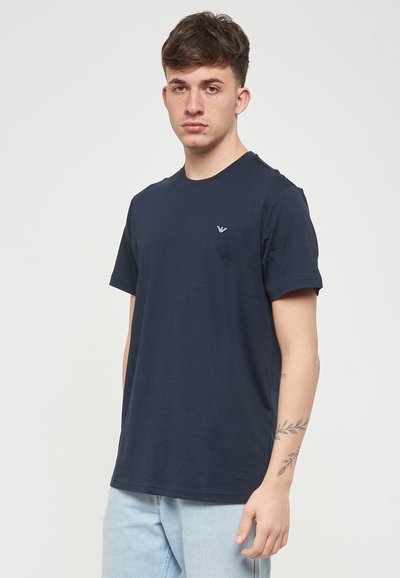 T-shirt bleu marine à col rond en coton, avec des manches courtes et un petit logo de marque sur la zone gauche de la poitrine.