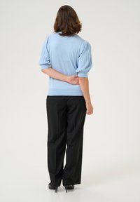 Pull en tricot bleu clair avec des manches bouffantes côtelées, associé à un pantalon large noir. La vue de dos montre une taille ajustée et une texture lisse.