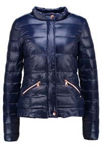 Mörkblå puffjacka med glänsande, quiltad textur, ståkrage och två framsidans dragkedjor med roséguldiga detaljer.