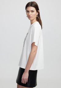 Camiseta blanca de algodón con un corte relajado y mangas cortas, que presenta un diseño gráfico texturizado en la parte delantera, combinada con una falda mini de cuero negra.