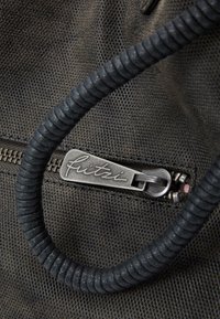 Černá taška z texturované látky s černou spirálovou rukojetí a stříbrným kovovým zipem, na kterém je vyryto jméno značky "fritzi".