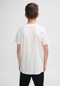 Hvid bomulds t-shirt med korte ærmer, rund halsudskæring og en afslappet pasform, set fra ryggen, parret med sorte bukser.