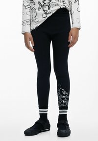 Fekete leggings, fehér Mickey Mouse grafikával az als�ó lábszáron, csíkos szegéllyel. Puha, rugalmas anyag. Figyelemre méltó textúra és mintázat részletek.