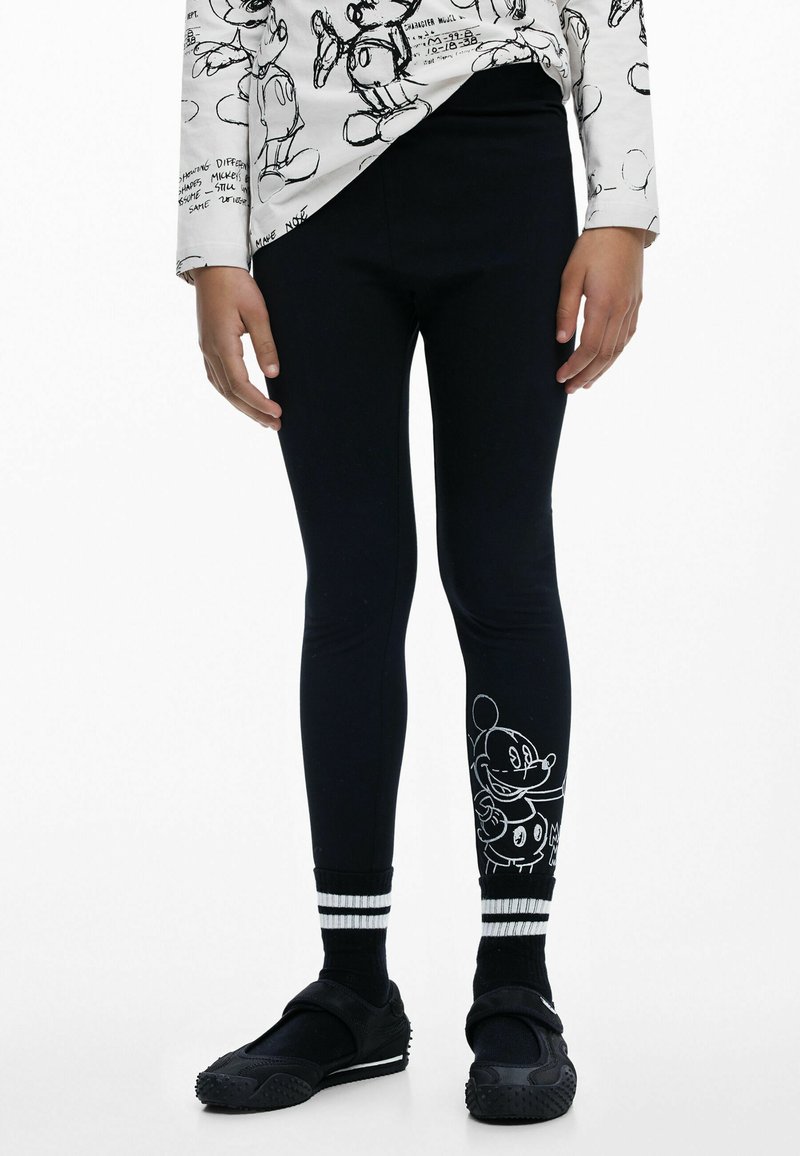 Fekete leggings, fehér Mickey Mouse grafikával az alsó lábszáron, csíkos szegéllyel. Puha, rugalmas anyag. Figyelemre méltó textúra és mintázat részletek.