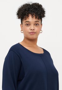 Μπλούζα ναυτικού μπλε, με μακριά μανίκια, φτιαγμένη από μαλακό ύφασμα, με στρογγυλή λαιμόκοψη και ραφές. Απλός σχεδιασμός με χαλαρή εφαρμογή.