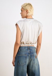 Cropped, light gray top with rolled sleeves and elastic hem; paired with high-waisted, blue denim jeans featuring back pockets.