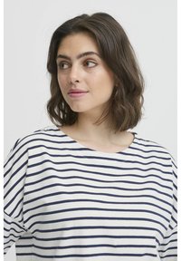 Tricou în dungi alb și bleumarin, cu un decolteu larg și mâneci scurte. Material moale cu o croială lejeră și un model cu dungi orizontale.
