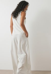 White, striped sleeveless top paired with loose, white, wide-leg pants. Fabric appears smooth with vertical pinstripes. Pockets included.