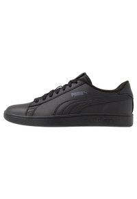 Scarpe in pelle nera con texture liscia, punta tonda e design con lacci. Presentano un logo Puma grigio di lato e una suola in gomma piatta.