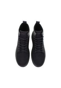 Pár černých šněrovacích ankle bot s polstrovanými límci a viditelným šitím, shlédnuto zvrchu na bílém pozadí.