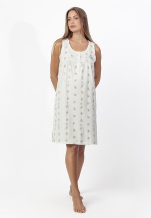 Mujer de pie descalza que lleva un vestido blanco sin mangas hasta la rodilla con pequeños patrones florales y de globos.