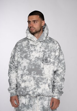Man wearing gray and white tie-dye hoodie and matching pants, with a skeleton hand graphic and "MULTIPLY" text on the chest.