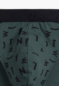 Ciemnozielona bawełniana bielizna z czarnym elastycznym paskiem uwydatnionym napisem "ATLANTIC" oraz wzorem różnych czarnych liter i symboli.