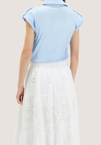 Blusa azzurro chiaro a maniche corte con colletto classico, abbinata a una gonna bianca a strati caratterizzata da motivi floreali ricamati.