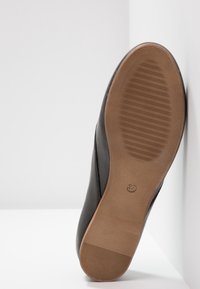 Semelle de chaussure en cuir noir avec un dessous en caoutchouc marron texturé, affichant la taille 37 et des rainures horizontales pour une meilleure adhérence.