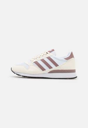Light-colored sneaker with fabric and suede materials, featuring three burgundy stripes, a white sole, and a cushioned collar.