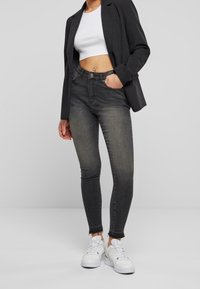 Czarne wysokie jeansy skinny z wyblakłym wykończeniem, strzępionym dołem i pięcioma kieszeniami, zestawione z krótką białą bluzką i żakietem.