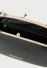 Svart läderkuvertväska med guldfärgad metallram, utrustad med ett lås och ett innerfack med dragkedja. Märkeslogotyp synlig.