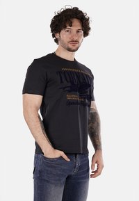 Camiseta de algodón negra con estampado gráfico de aeronaves militares, cuello redondo, mangas cortas y ajuste relajado, combinada con jeans azules.