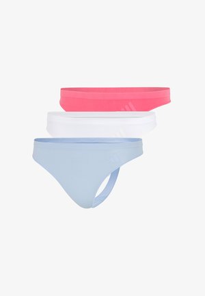 Jonge vrouw met gevlochten haar, gekleed in een lichtblauwe sportbeha en bijpassende bikinionderdelen, staand op blote voeten tegen een effen achtergrond.