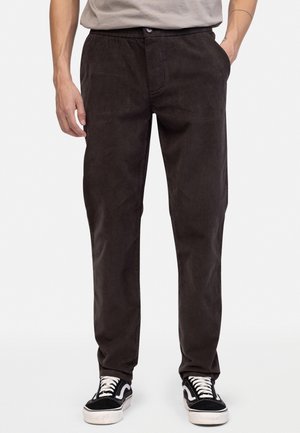 Zwarte corduroy broek met een elastische tailleband en zijzakken, met een relaxte pasvorm en een soepele textuur. Gecombineerd met zwarte sneakers.