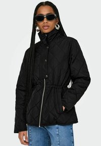Veste noire matelassée avec un col haut, une taille élastique et une fermeture éclair à l'avant. Comprend des boutons-pression et des poches latérales pour une utilité supplémentaire.
