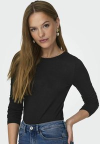 Svart langermet topp med rund hals, laget av glatt stoff. Kombinert med blå jeans med knapplukking og frontlommer.