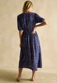 Šaty po kolená s kvetinovým vzorom v námorníckej modrej farbe, s krátkymi balónovými rukávmi a s priliehavým pásom. Tkanina sa zdá byť ľahká a splývavá.