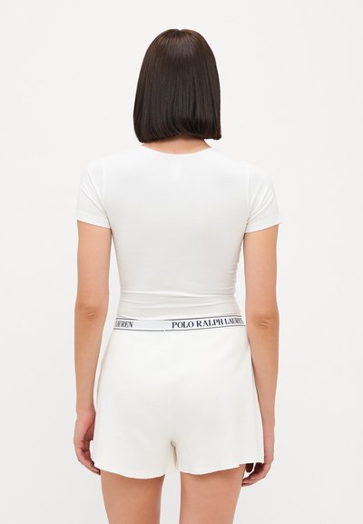 White fitted t-shirt with short sleeves paired with white shorts featuring a textured fabric and a waistband marked "POLO RALPH LAUREN."