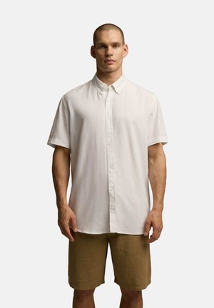 Biała koszula z krótkim rękawem, z kołnierzykiem zapinanym na guziki i subtelną teksturą, w połączeniu z beżowymi szortami. Odpowiednia do codziennego użytku.