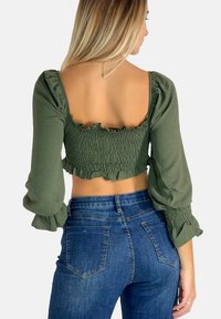 Olivengrøn cropped top med smock-design, flæseaccenter og puffærmer, parret med højhalsede denimjeans.