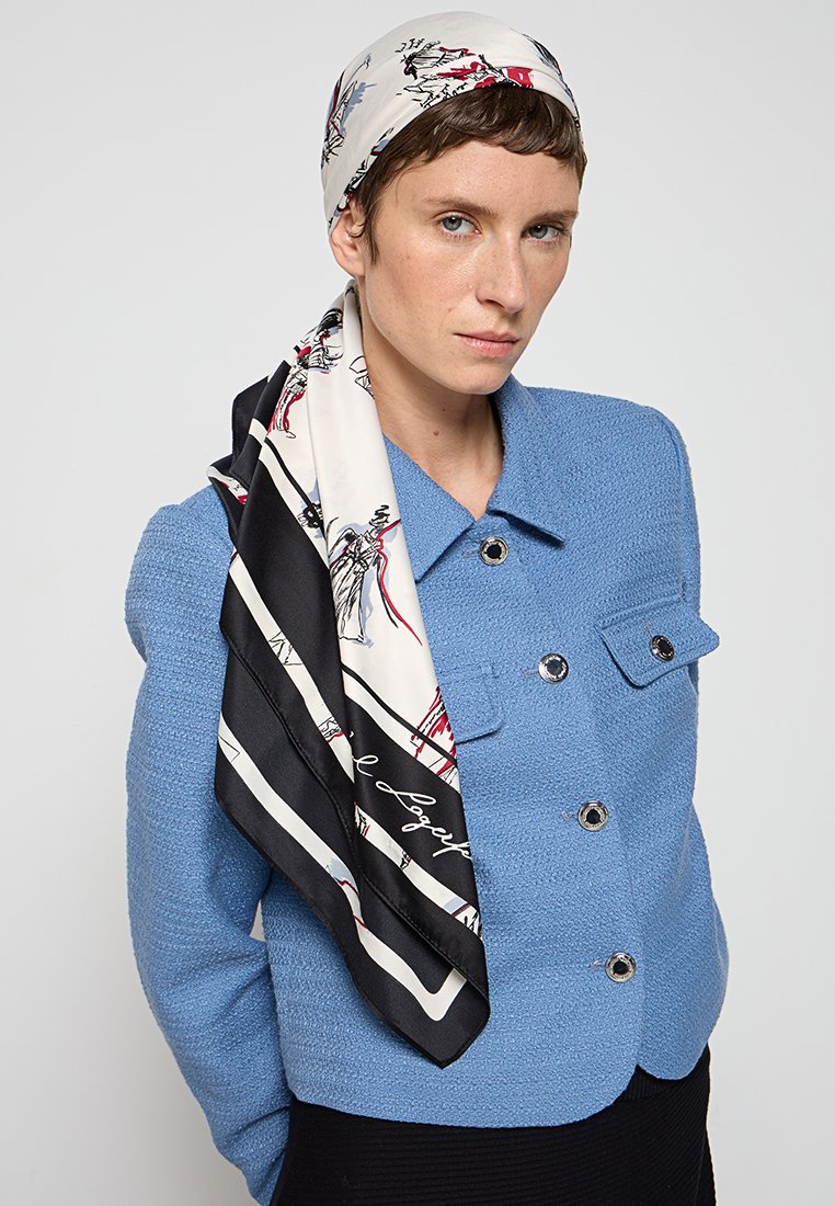 Foulard di seta con sfondo bianco e illustrazioni rosse e blu, bordato di nero, adagiato su una giacca testurizzata di colore blu chiaro con bottoni doppi.