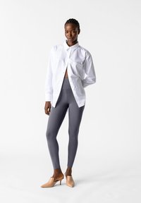 Camicia bianca con bottoni, leggings grigi e mule beige con tacco. La camicia ha una tasca singola ed è leggermente sbottonata in vita.