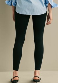 Fekete leggings sima textúrával és testhezálló megjelenéssel, világoskék csíkos pólóval és fekete tűsarkú szandállal párosítva.