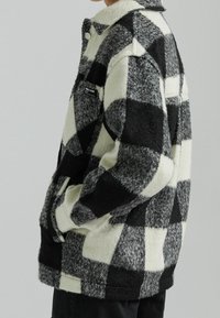 Svart och vit rutigt fleecejacka med knappäged krage, sidofickor och bröstficka. Mjuk textur, oversize passform och kontrasterande mönster.