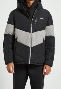 Giacca a vento imbottita con design a chevron in nero e grigio, con chiusura frontale a zip, cappuccio e dettagli di cucitura a vista. Logo sul petto.