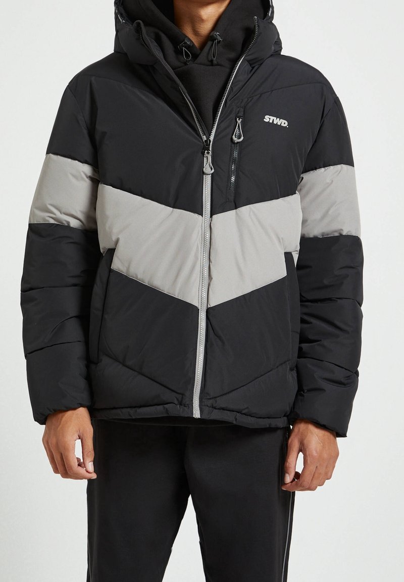 Giacca a vento imbottita con design a chevron in nero e grigio, con chiusura frontale a zip, cappuccio e dettagli di cucitura a vista. Logo sul petto.