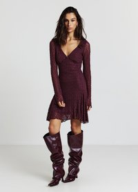 Bordeauxrotes Spitzenkleid mit langen Ärmeln, V-Ausschnitt und ausgestelltem Saum; kombiniert mit kniehohen, lässigen burgunderfarbenen Stiefeln. Strukturierte Stoffdetails sichtbar.