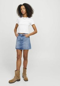 Hvit cropped t-skjorte, blå denim A-line skjørt og lysebrune semskede ankelsko med spenner. Skjørtet har et klassisk fem-lomme-design.