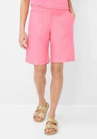 Roze linnen shorts met twee achterzakken en een relaxte pasvorm, gecombineerd met slide-sandalen in meerdere kleuren met decoratieve gespen.