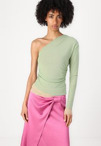 Asymmetrical one-shoulder top in light green, layered with a nude section, paired with a pink wrap skirt featuring a knotted detail.