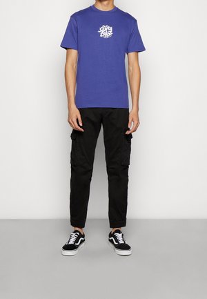 Camiseta de algodón azul real con estampado gráfico blanco en el pecho, combinada con pantalones cargo negros con bolsillos laterales y zapatillas negras.